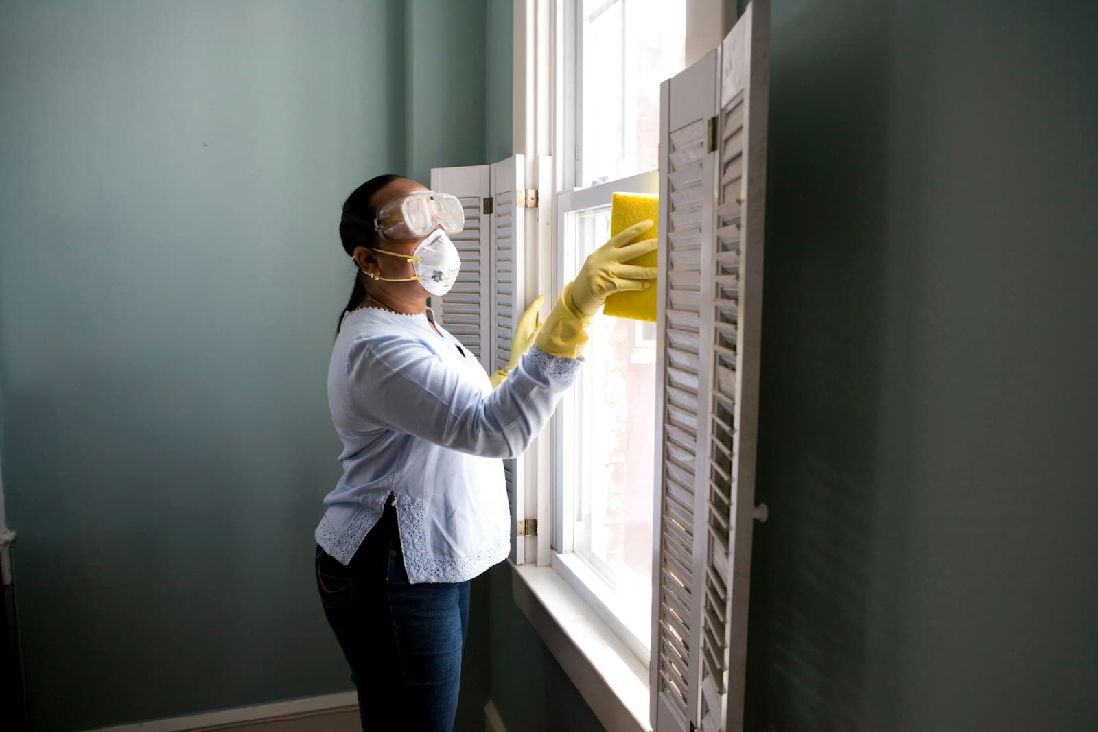 A cleaner wiping down a window in a bright home