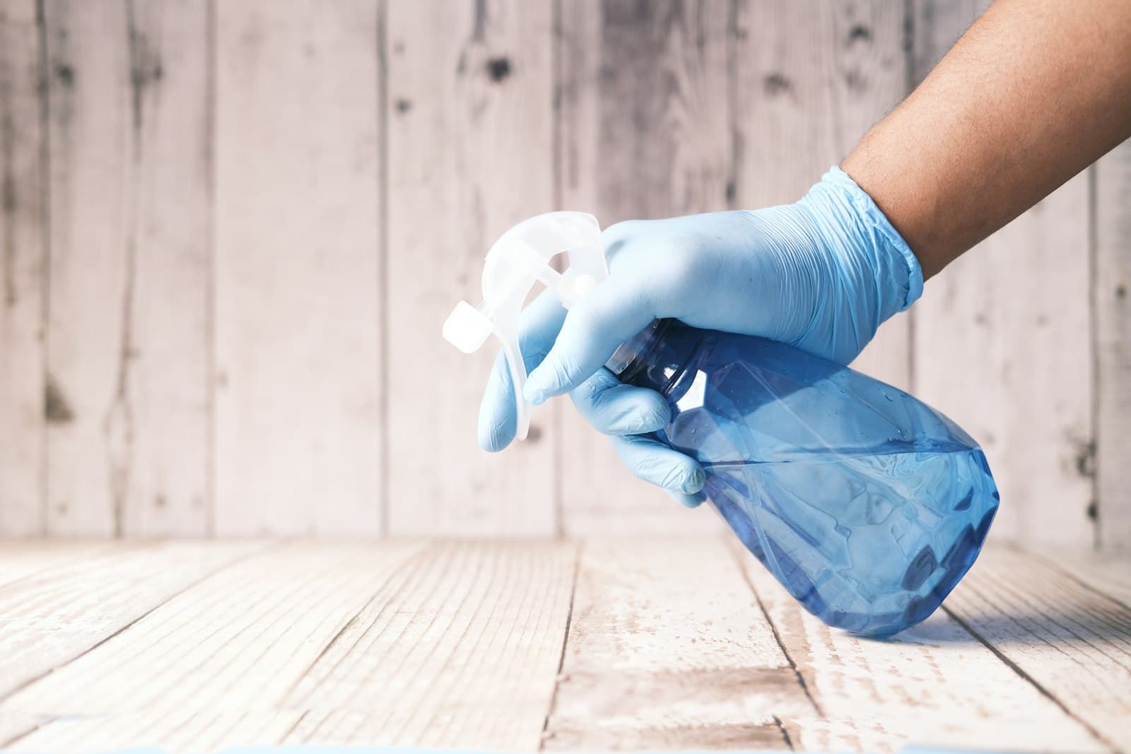 Gloved hand holding a blue spray bottle